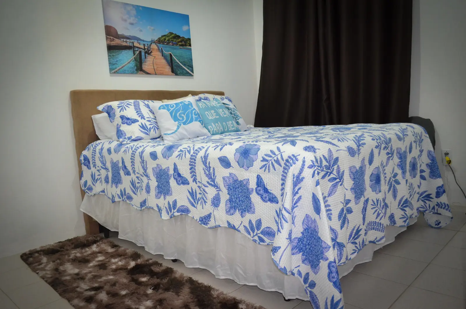 Quarto Borboletas com colcha azul e branca, quadro do píer e cortina blackout